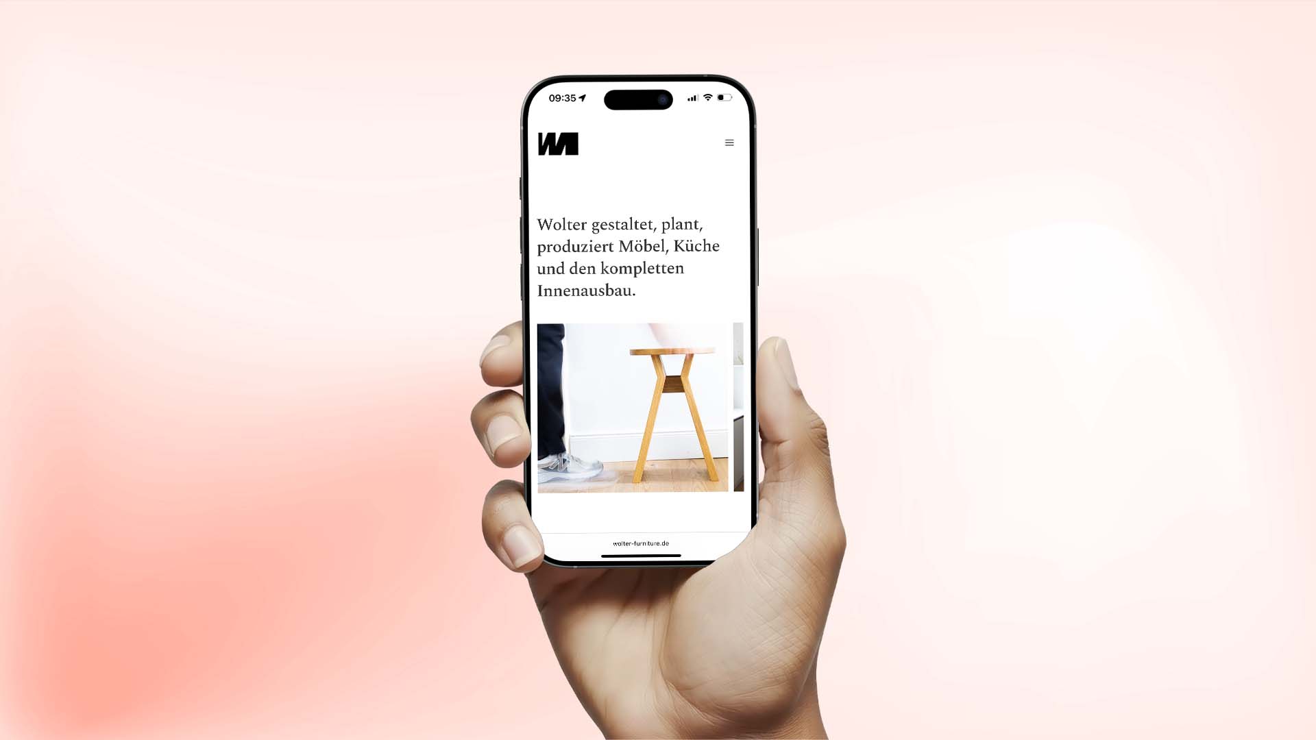 Hand hält ein Smartphone, auf dem die mobile Website von Wolter Furniture mit Text zu Möbel-, Küchen- und Innenausbauleistungen sowie einem Foto eines Holzhockers zu sehen ist.