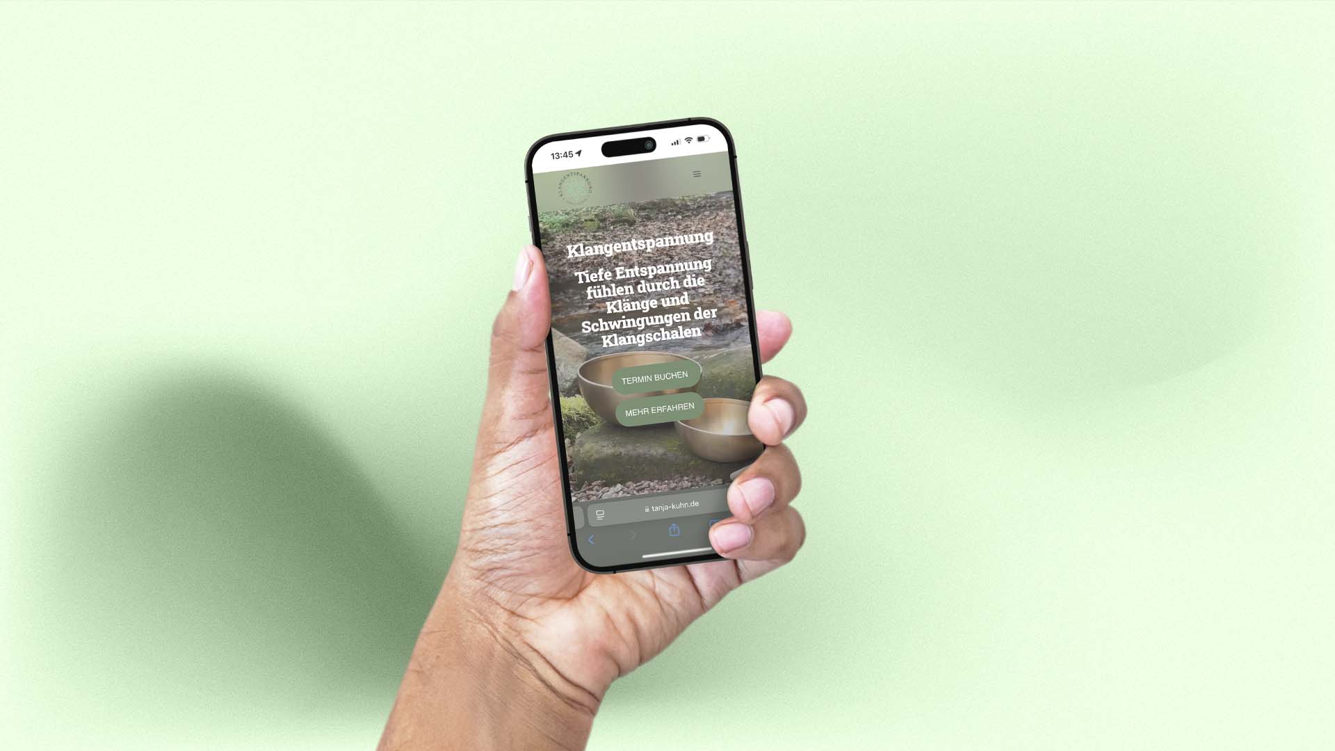Hand hält ein Smartphone, auf dem die mobile Website von Tanja Kuhn mit der Überschrift Klangentspannung und den Buttons Termin buchen und Mehr erfahren zu sehen ist.